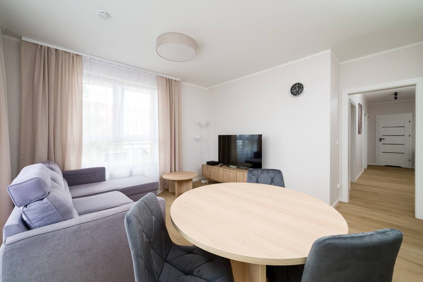 Una sala de estar moderna con un sofá, una mesa de comedor redonda, un televisor y un reloj en la pared.