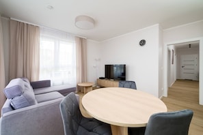 A modern living room with a sofa, a round dining table, a television, and a clock on the wall.
