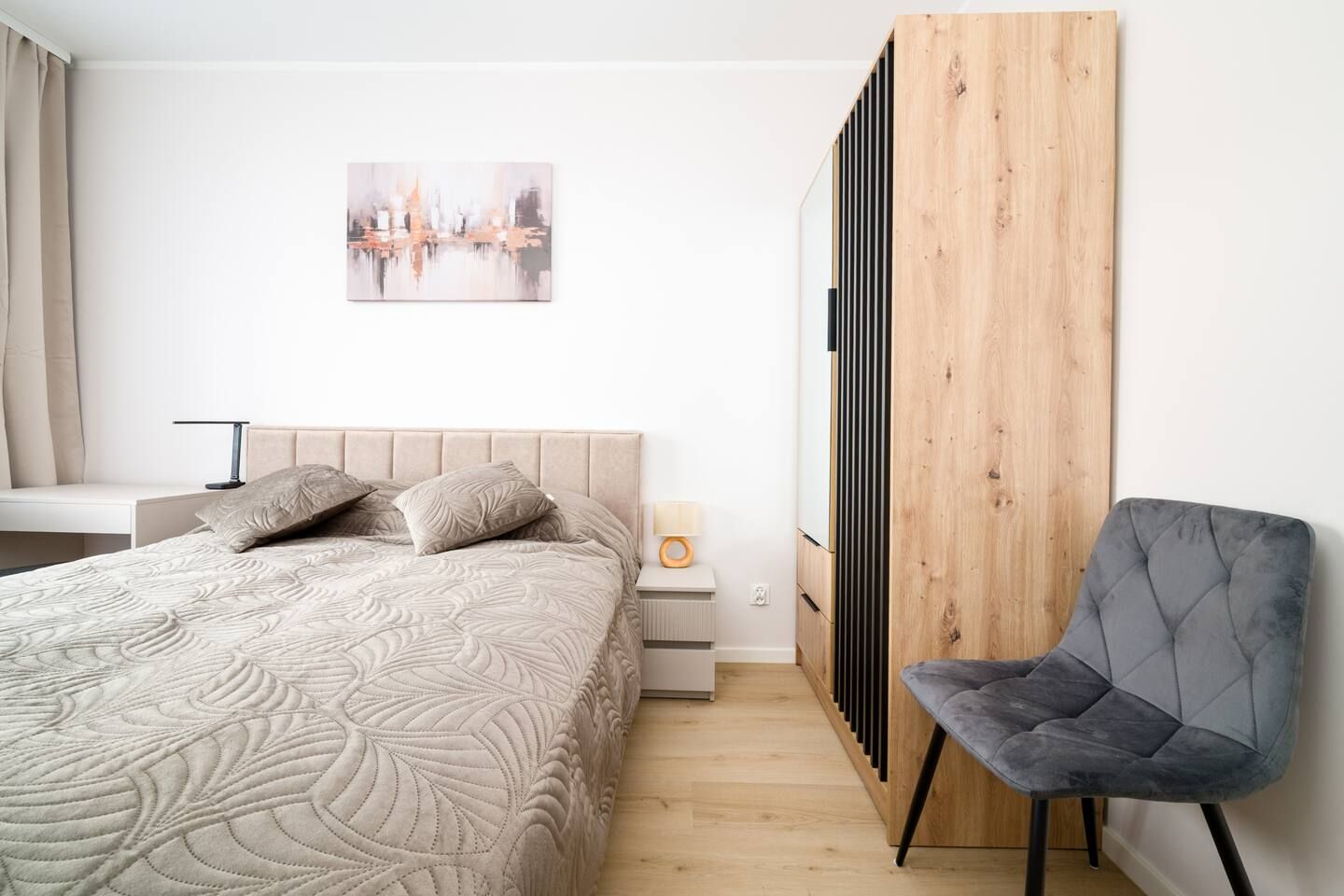 A bedroom with a bed, a chair, a bedside table, a lamp, and a painting on the wall.