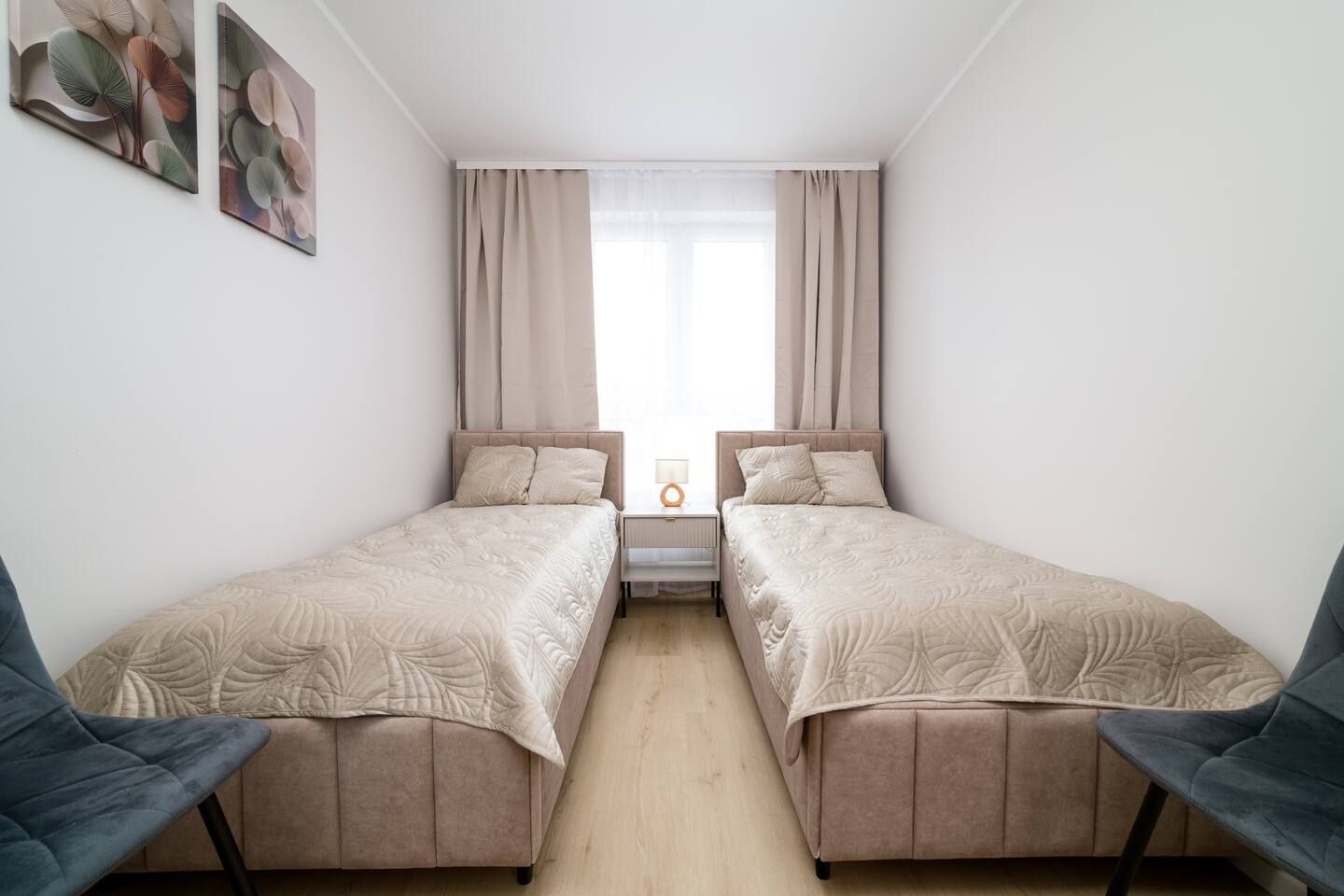 Een slaapkamer met twee bedden, een nachtkastje, een lamp en een raam met gordijnen.