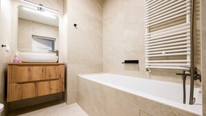 A modern bathroom with a freestanding bathtub, a wooden vanity, a mirror, and a towel rack. - Wrocław Three-Bedroom Apt — Parking, A/C & Balcony (Wrocław)