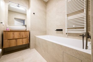 Un bany modern amb una banyera autònoma, un tocador de fusta, un mirall i un suport per a tovalloles.