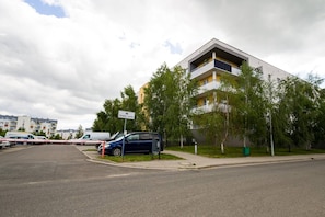 A multi-story residential building with a flat roof, a parking area with several cars, and a street sign indicating the name 'Strefa ruchu'.