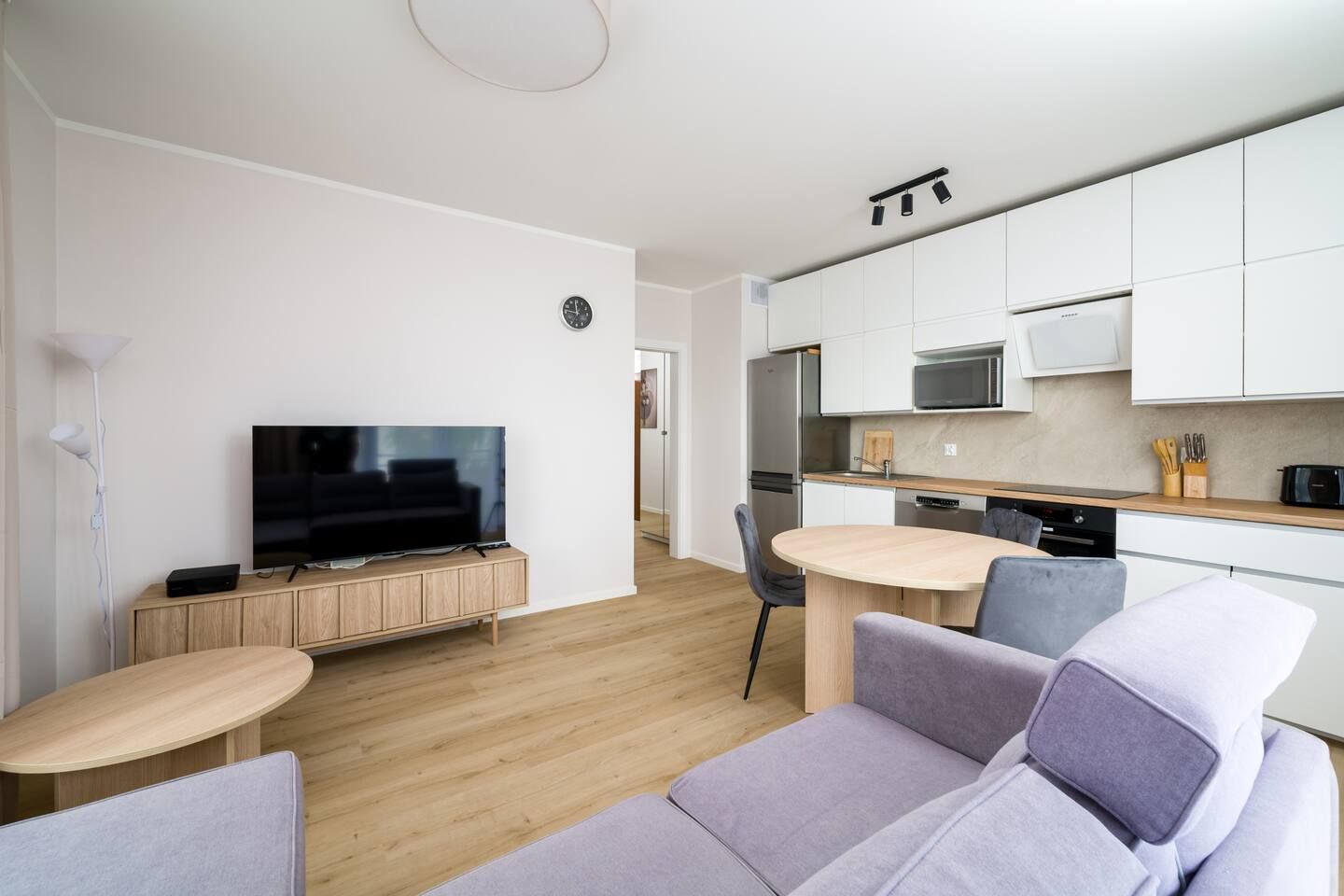 A modern apartment with a living area, a dining table, a kitchen, and a flat-screen TV.