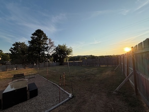 A fenced outdoor area with a gravel patio, a wooden fence, and a tree. - Razorback Retreat with Bunks & Game Room (Farmington)