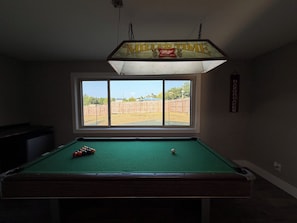 A pool table with a window view of a fenced yard. - Razorback Retreat with Bunks & Game Room (Farmington)