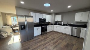 Cozinha moderna com armários brancos, eletrodomésticos de aço inoxidável e piso de madeira em padrão herringbone.