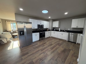 Une cuisine moderne avec des armoires blanches, des appareils en acier inoxydable et un parquet en bois disposé en chevrons.
