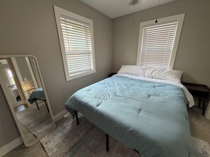 A bedroom with a bed, two windows with blinds, a mirror, and a ceiling fan. - Razorback Retreat with Bunks & Game Room (Farmington)