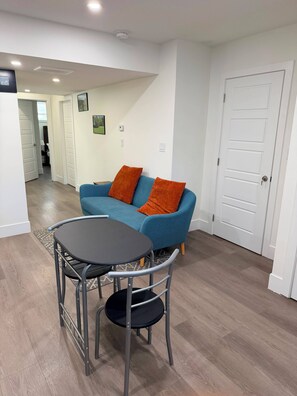 Un salon moderne avec un canapé bleu, deux coussins orange, une table ronde et une chaise.