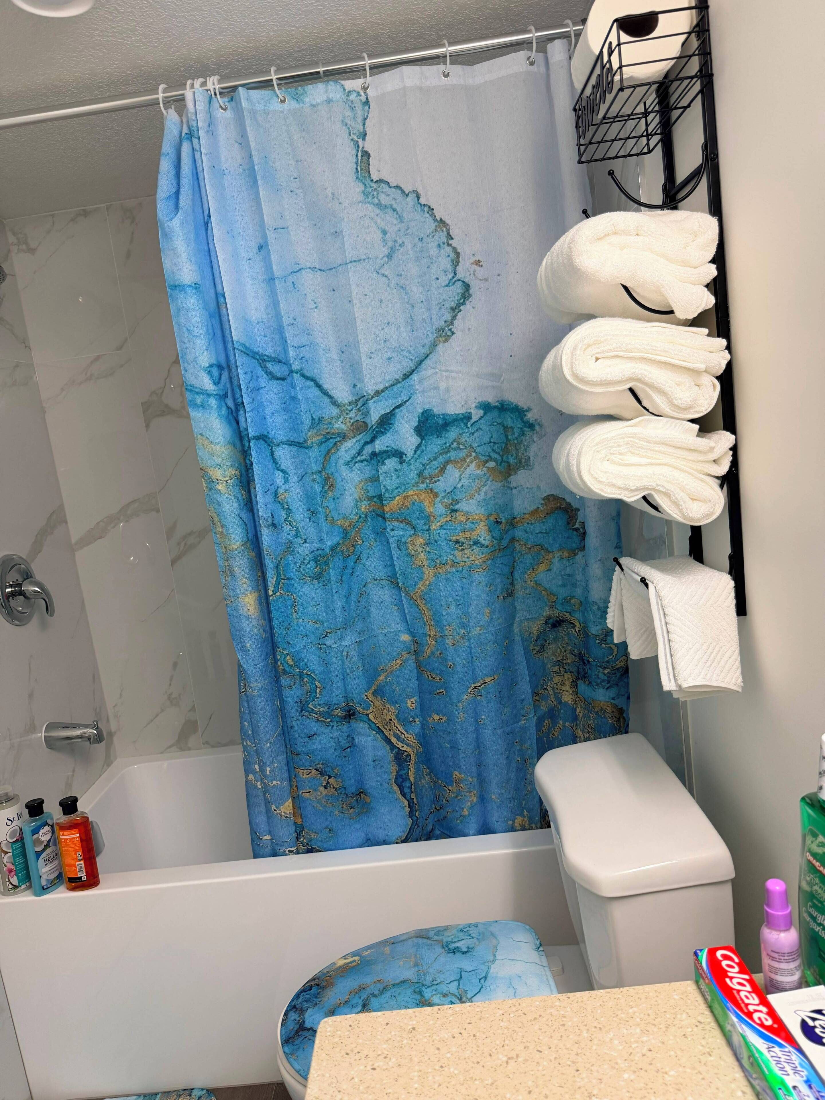 Une salle de bain avec un rideau de douche en marbre bleu, des toilettes blanches et un porte-serviettes avec des serviettes pliées.