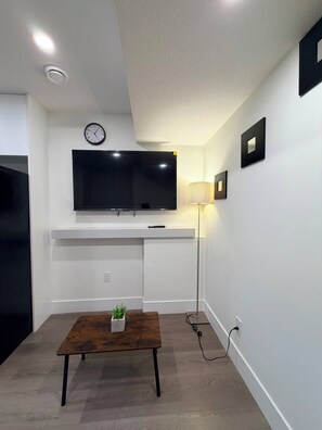 Un salon moderne avec un téléviseur à écran plat fixé au mur, une table basse agrémentée d’une plante et un lampadaire.