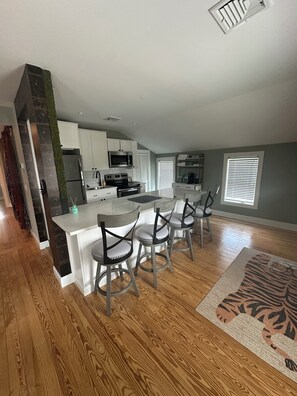 A modern kitchen with white cabinets, a central island, and bar stools. -  3 BR apartment with central AC in the village. Steps to Main St. (Westhampton Beach)