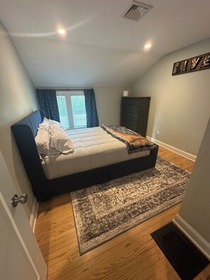 Une chambre à coucher avec un lit, un tapis, une commode et une fenêtre avec des rideaux.