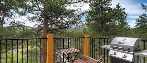 Une terrasse dotée d’un barbecue et de sièges, entourée d’arbres et offrant une vue sur le paysage.