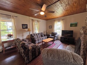 A living room with a ceiling fan, a sofa set, a television, and a fireplace. - Large Verandah, lake views, 4 bedroom historic cottage, the Annex. Clyffe House (Port Sydney)