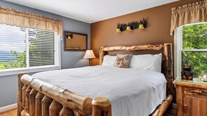 A bedroom with a large bed, wooden headboard, a bedside lamp, and a window with blinds. - Bear Ridge by Avantstay Smoky Views + Indoor Pool + Sauna & Spa Near Park Trails (Gatlinburg)