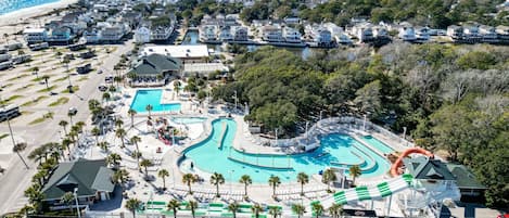 Vista aérea de un complejo turístico con una amplia piscina, propiedades frente a la playa y un estacionamiento.