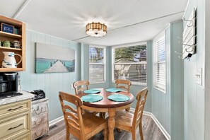 A dining area with a round wooden table, four chairs, and a ceiling light fixture. - Saltwater Shanty GolfCart•Linens•OceanLakes (Horry County)