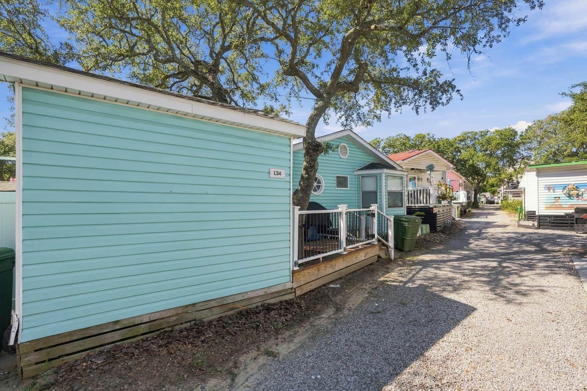 A row of mobile homes with a gravel driveway and trees in the background.
