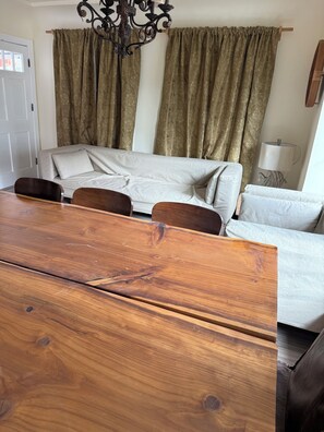 A living room with a sofa, a wooden dining table, and curtains.