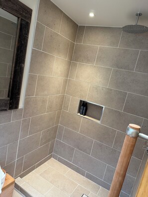 A shower area with beige tiles, a wooden handrail, and a shelf with toiletries.