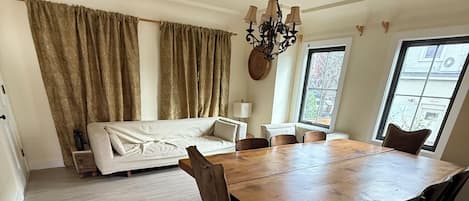A dining area with a wooden table and chairs, a sofa, and a chandelier.