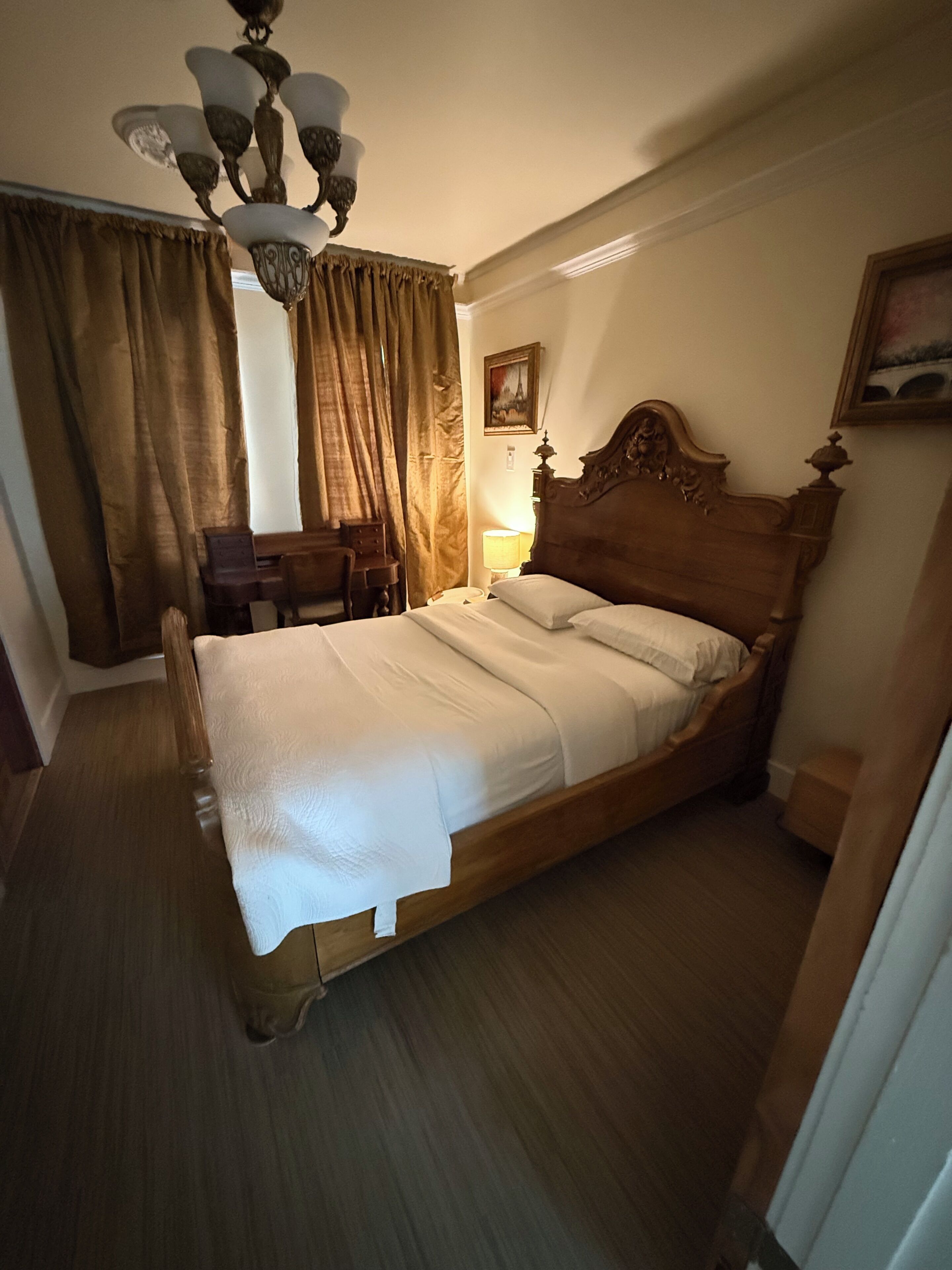 Ein Hotelzimmer mit einem hölzernen Bett, einem Schreibtisch, einem Stuhl, einer Lampe und einem Bild an der Wand.