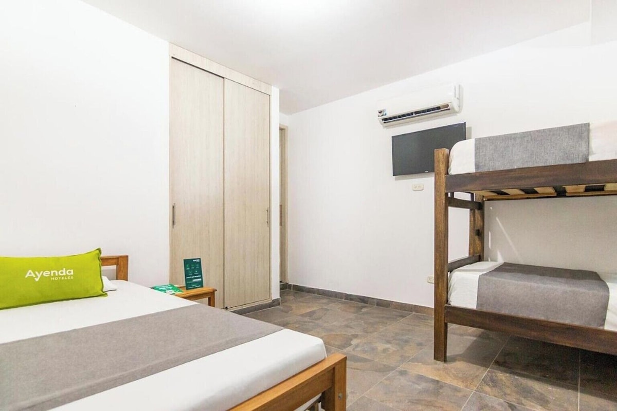Een hotelkamer met een stapelbed, een eenpersoonsbed met een groen kussen, een houten garderobe, een flatscreen televisie aan de muur en een klein tafeltje met een groen bordje.