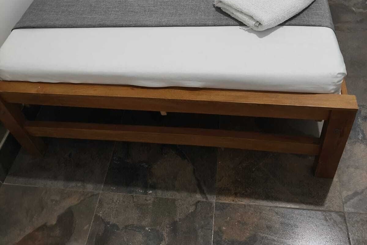 Een bed met een houten frame, wit beddengoed en een grijze deken.