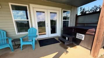 A covered outdoor area with two blue chairs, a barbecue grill, and a sign instructing to wipe feet before entering.