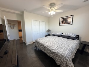 Un dormitorio con una cama, un ventilador de techo, un reloj en la pared y una puerta que da a otra habitación.