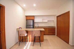 A compact kitchen with a built-in refrigerator, a sink, and two bar stools. - Makeva: Ocean View Steps from the Beach (Mazatlán)