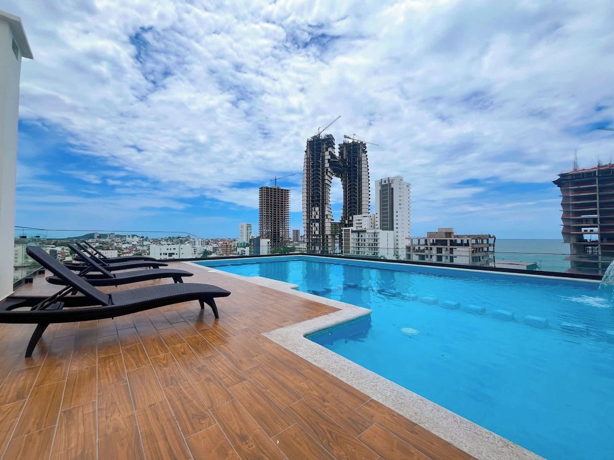 A rooftop pool area with lounge chairs and a view of a cityscape with modern buildings.