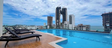 Un espace piscine aménagé sur le toit, avec des chaises longues et une vue sur le paysage urbain, dominé par des bâtiments modernes.