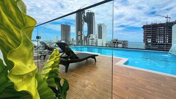 A rooftop pool with a city skyline view, lounge chairs, and a wooden deck.