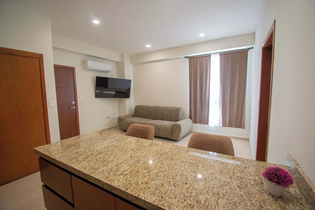 A modern kitchen with granite countertops, a built-in oven, and a flat-screen TV mounted above the oven.