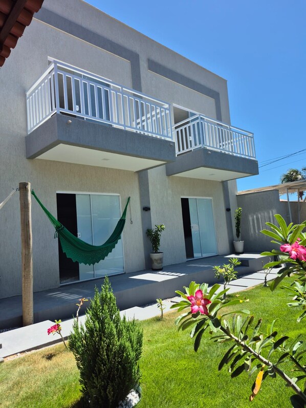 A modern two-story building with balconies, a hammock, and potted plants.