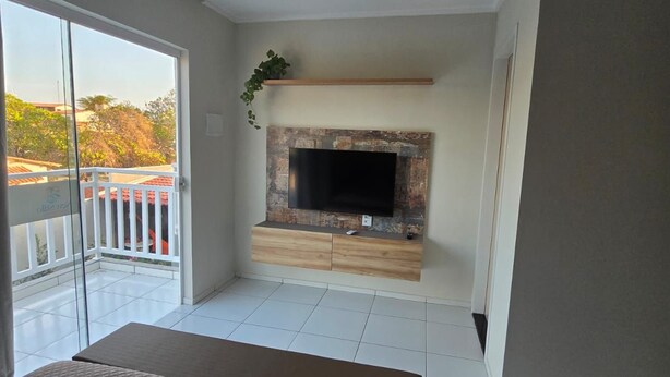 A room with a bed, a TV mounted on a stone wall, and a balcony with a view. - Residencial New Stilo (Aracati)