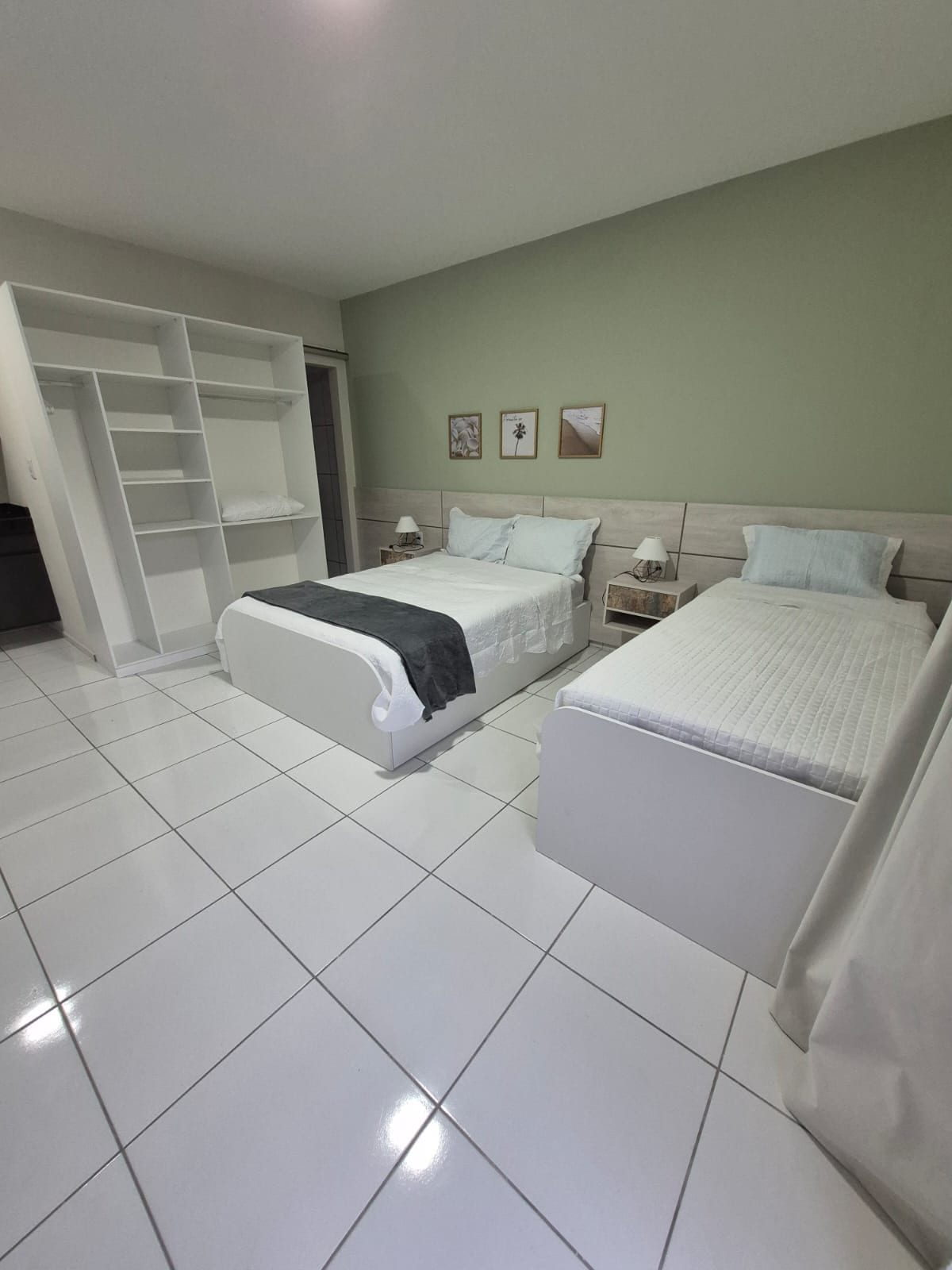 A hotel room with a large bed, a smaller bed, a wardrobe, and a nightstand with a lamp.