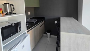 A compact kitchen with a microwave, kettle, and a small trash bin. - Residencial New Stilo (Aracati)