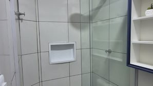 Ein kleiner, abgeschlossener Duschbereich mit Glastür, einem weißen Waschbecken und einer Toilette.