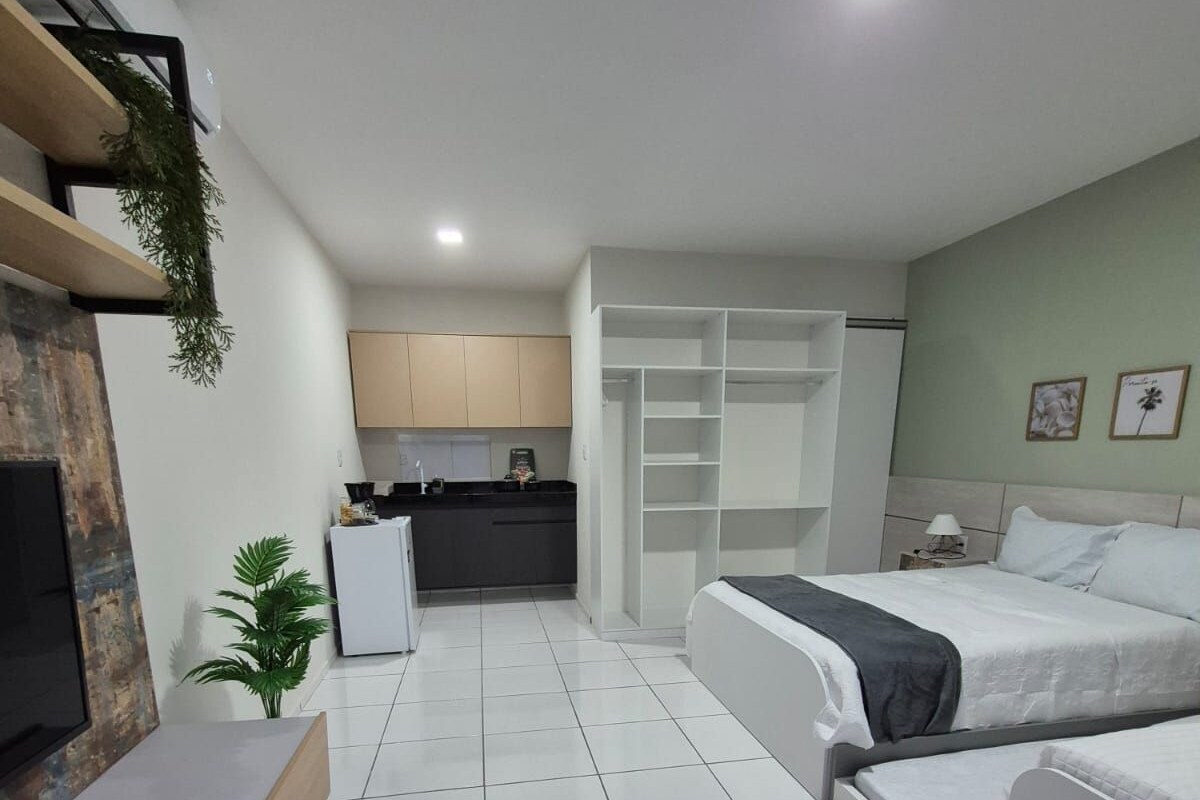A modern hotel room with a bed, a TV, a desk, and a kitchenette.