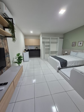 A modern hotel room with a bed, a TV, a desk, and a kitchenette. - Residencial New Stilo (Aracati)
