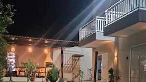 Ein gut beleuchteter Außenbereich mit Rasenfläche, einer überdachten Terrasse und einer Treppe, die zu einer oberen Ebene führt.