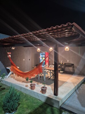Un patio cubierto con una hamaca, plantas en macetas, un comedor y una barra.