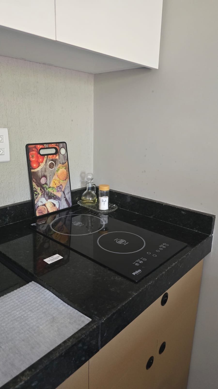 A kitchen with a black induction cooktop, a smartphone with a food-themed case, a glass container, and a small bottle.
