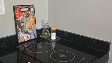 A kitchen with a black induction cooktop, a smartphone with a food-themed case, a glass container, and a small bottle.