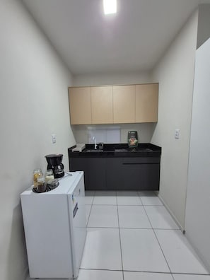 A compact kitchen with a refrigerator, a coffee maker, and a sink. - Residencial New Stilo (Aracati)