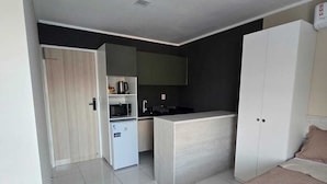 A compact bedroom with a bed, a small kitchenette, and a wardrobe. - Residencial New Stilo (Aracati)